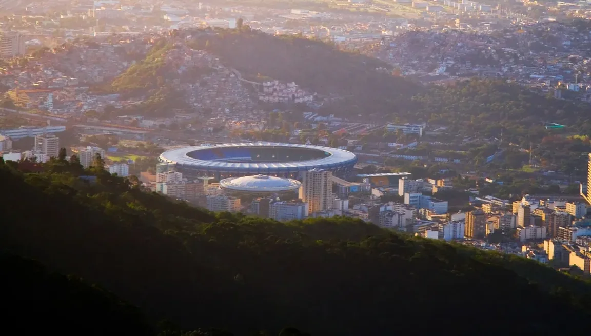 Estádio visto de longe, com a cidade e o pôr do sol ao fundo