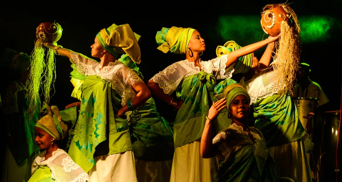 Bailarinos em figurinos coloridos durante apresentação no palco